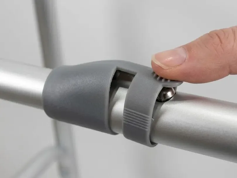 Close-up of the walking frame's central single-button fold mechanism on the top cross-bar.