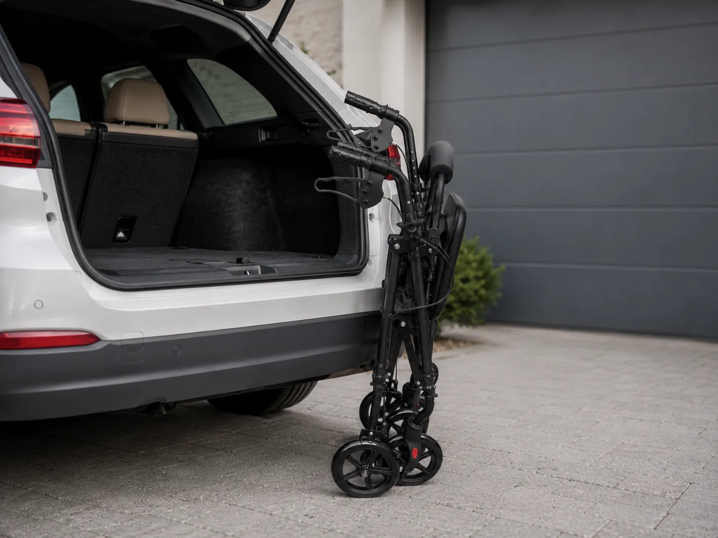 The EazyFold rollator folded to a slim 24 cm width, standing beside a car boot ready for transport.