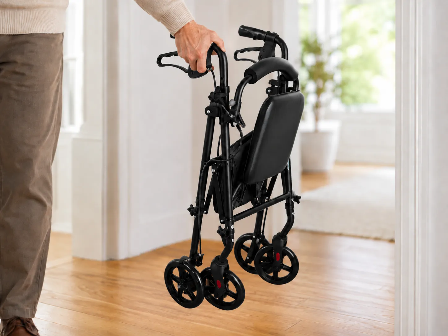 A hand lifting the folded lightweight EazyFold rollator one-handed, showing its 5.7 kg aircraft-grade aluminium frame.