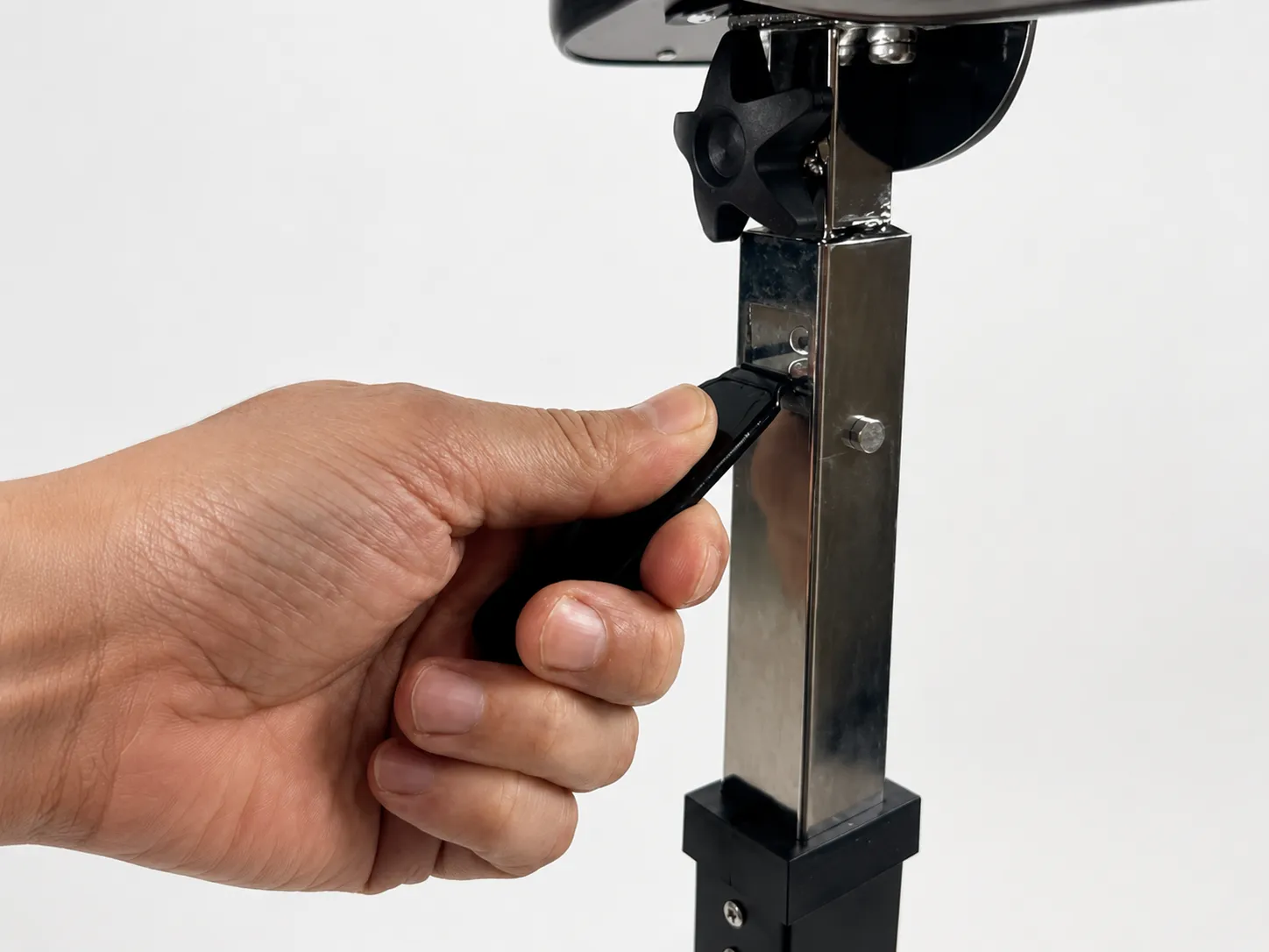 A hand squeezing the gas-release lever beneath the U-Base overbed table's top to adjust its height.
